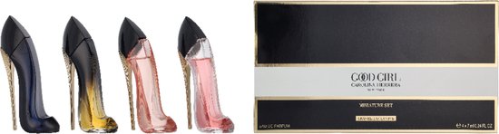 Vier glazen schoenflessen met hoge hakken, met een parfumflesje in het donkerblauw, goud-zwart ombré, en twee lichtroze, naast een zwarte geschenkdoos met gouden strepen en 'Good Girl' erop.