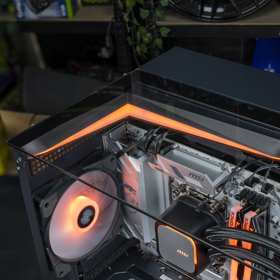 Gaming pc met oranje verlichting. Links een ventilator, rechts de moederbord met MSI koeler. Glazen zijkant.