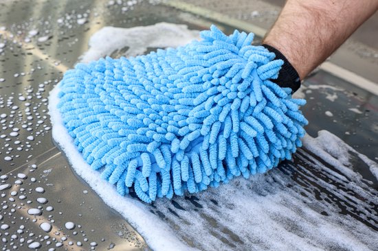 Close-up van een blauwe chenille microvezel washandschoen die een nat, schuimend oppervlak van een auto schoonmaakt.