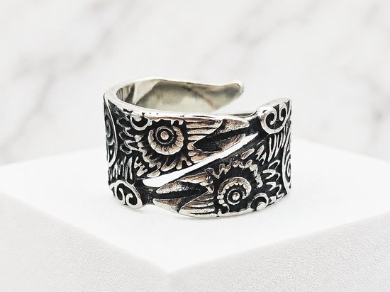 Zilverkleurige ring met Viking Raven patroon, op een witte kubus.