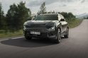Donkergroene SUV rijdt op een landweg door een bosrijk gebied, gefotografeerd vanaf de voorkant.