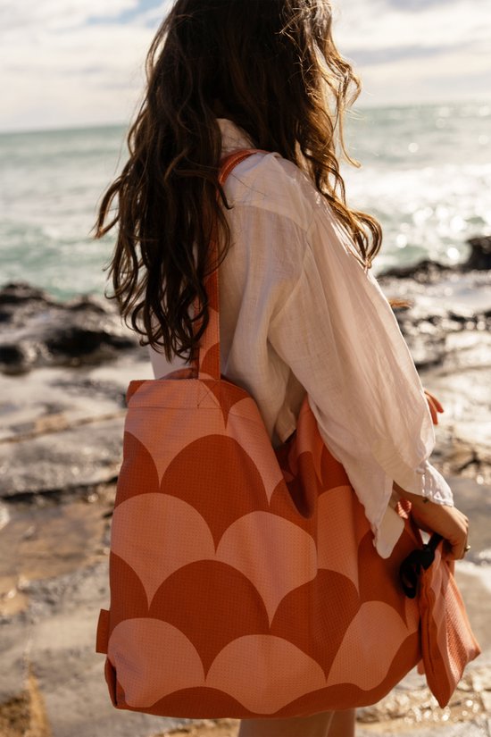 Een vrouw met lang bruin haar draagt een witte blouse en een grote, oranje tas met cirkelpatroon aan haar schouder.