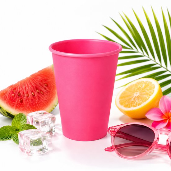 Roze kartonnen beker met zomers fruit, zonnebril en ijsblokjes op een witte achtergrond.
