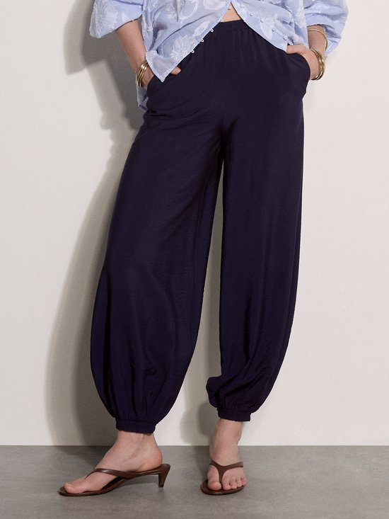 Detail van model in losvallende blauw gestreepte blouse met bloemenpatroon en donkere ballonbroek.