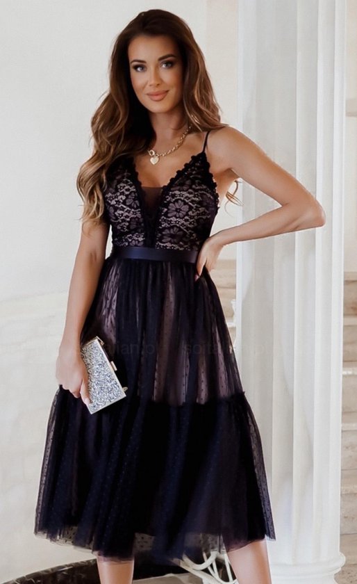Une femme porte une robe midi noire avec un corsage en dentelle et des détails en dentelle sur la robe. La robe a des bretelles fines et un nœud à la taille.