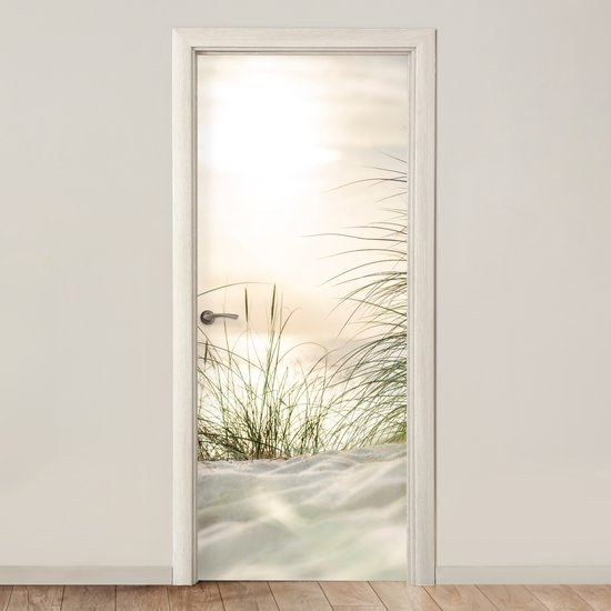 Een deursticker met een zonsondergang boven de duinen, zand en wuivend gras.