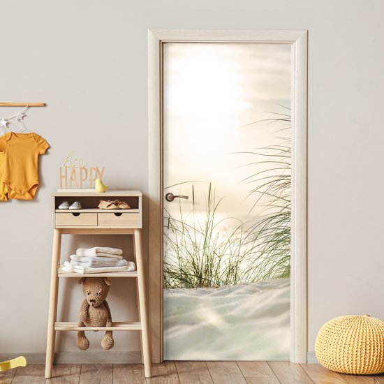 Deurposter met zandduinen en grassprieten bij zonsondergang, met een gele poef op de voorgrond.