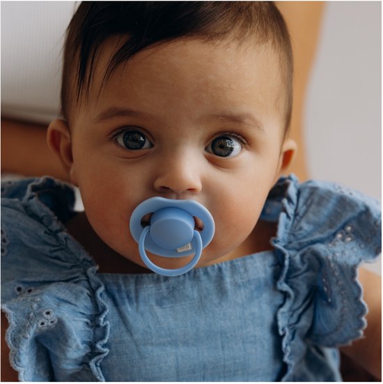 Baby met een blauwe speen in een blauwe outfit.
