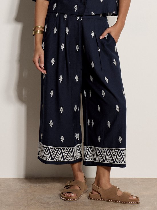 Marineblauwe culotte met witte diamantjes en geborduurde randen, gedragen met sandalen.