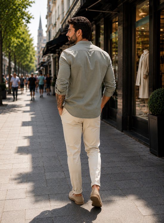Man loopt over straat met de rug naar de camera, draagt een lichtgroene linnen blouse met opgerolde mouwen en beige broek.