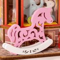 Roze houten hobbelpaardje met sierlijke uitsnijdingen, op een witte ondergrond.