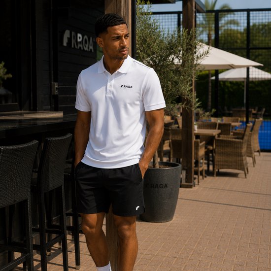 Man staat buiten, draagt witte Raqa® polo met korte mouwen en zwarte shorts. Logo op borst en short.