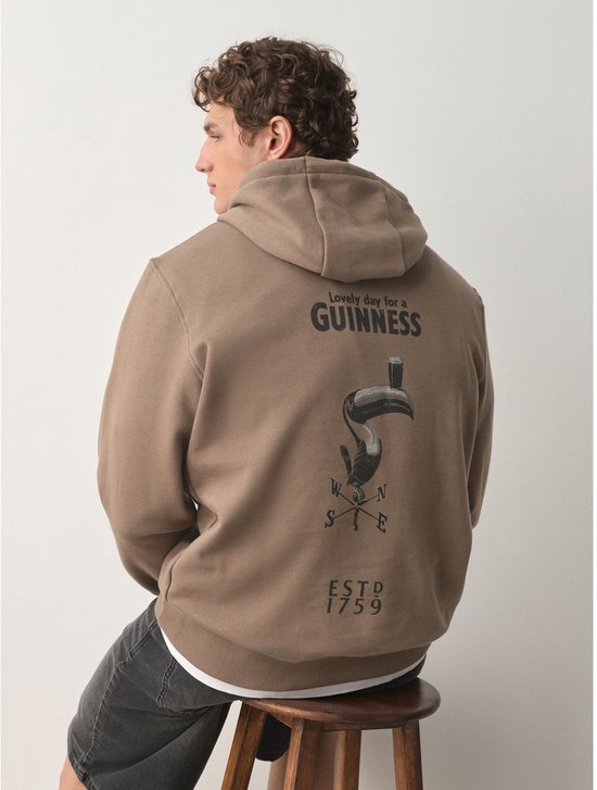 Man zittend op een stoel in bruine hoodie met opdruk 'Lovely day for a GUINNESS' op de rug.