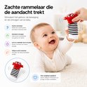 Rode lieveheersbeestje-rammelaar aan zwart-wit gestreept babysokje, vastgehouden door een hand boven een baby.