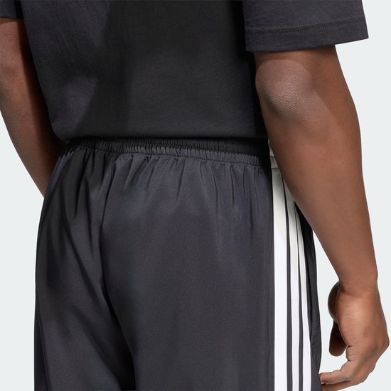 Gedetailleerde achterkant van een zwarte sportbroek met elastische tailleband en witte Adidas strepen.
