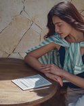 Een vrouw met gestreepte sjaal leest op een BOOX e-reader aan een houten tafel bij een stenen muur.