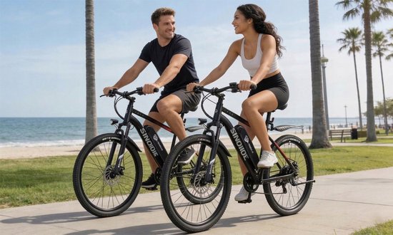 Man en vrouw in sportkleding rijden op zwarte elektrische mountainbikes langs het strand.