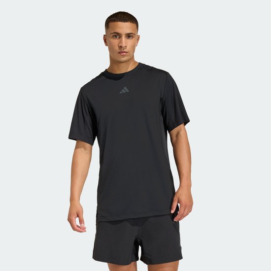 Man met zwart Adidas performance shirt met subtiel textuurpatroon en korte mouwen, gedragen met zwarte shorts.