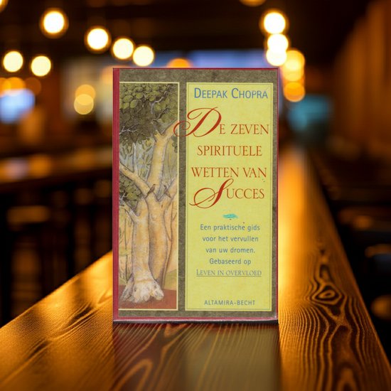 Boek met de titel 'De zeven spirituele wetten van succes' op een houten tafel, met bokeh-verlichting op de achtergrond.