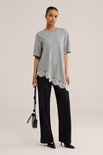 Model draagt een zwarte jersey broek met regular fit en een grijs, asymmetrisch shirt met kanten rand.