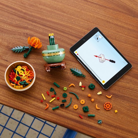 Pièces Lego, une tablette avec des instructions de construction, un bol de pièces et un chrysanthème Lego sur une table.