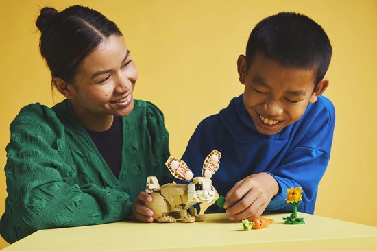 Femme et enfant construisent un lapin LEGO avec carotte.