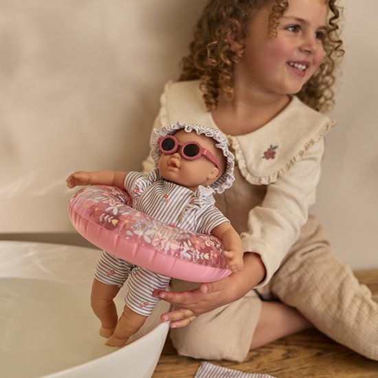 Meisje met een pop met gestreept zwempak, zwemband en zonnebril.