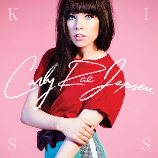 Carly Rae Jepsen voor een roze achtergrond in een rood T-shirt en turquoise rok met het woord KISS.