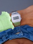 Zilverkleurig Casio horloge op de pols van een vrouw, gedragen met een felgroene top en gebloemde jeans.