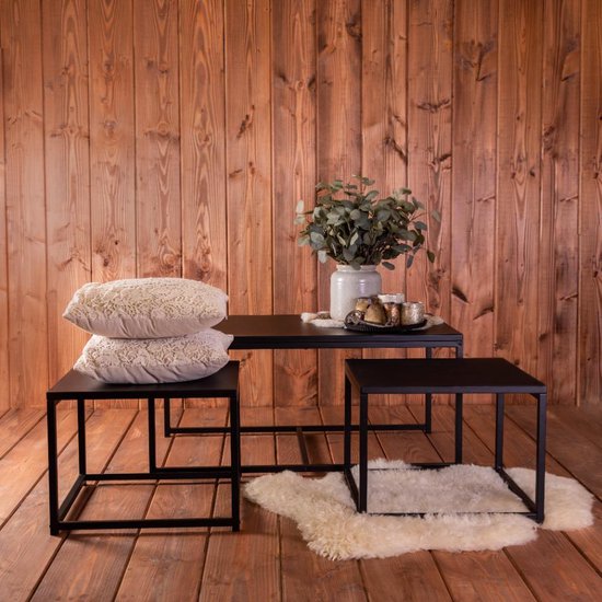 Ensemble de tables basses noires avec deux petites tables et une plus grande table sur un plancher en bois, avec des coussins et une peau de mouton.