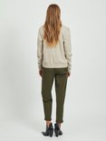 Model met haar rug naar de camera, draagt een beige gebreid vest en olijfgroene broek.