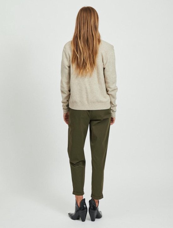 Model met haar rug naar de camera, draagt een beige gebreid vest en olijfgroene broek.