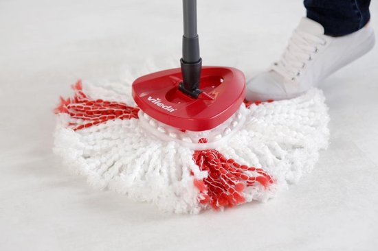 Une serpillère rotative blanche aux franges rouges avec un manche rouge Vileda, sur un sol blanc. Une basket blanche est visible.