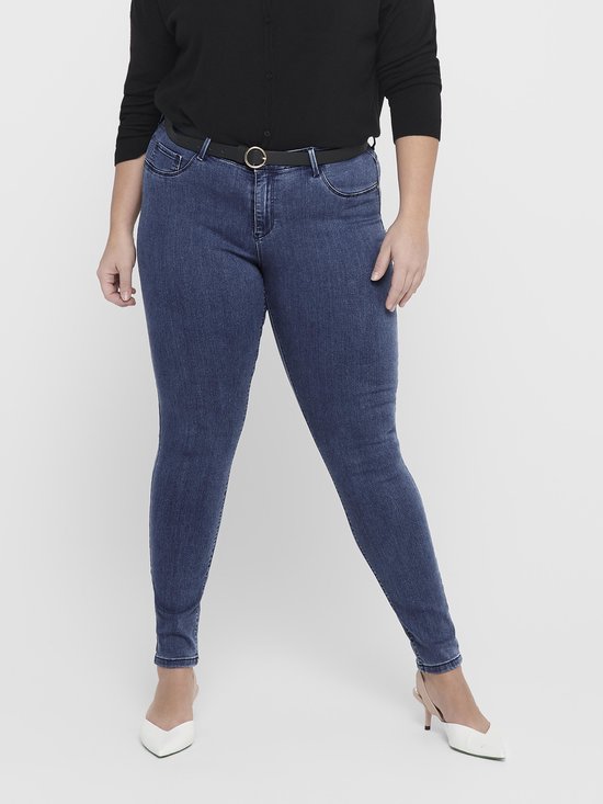 Blauwe skinny jeans, model draagt een zwarte cardigan en witte pumps.