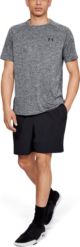 Man loopt met de hand in de zak van een zwarte korte broek en draagt een grijs gemêleerd sportshirt.
