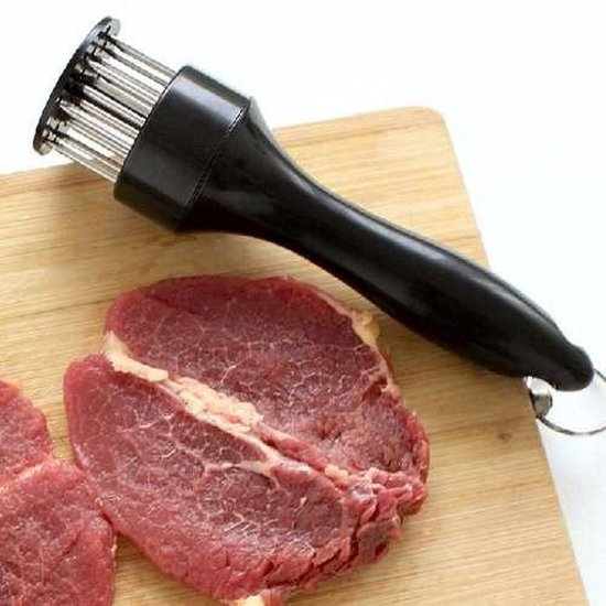 Attendrisseur à viande noir sur une planche en bois à côté de deux morceaux de viande crue.