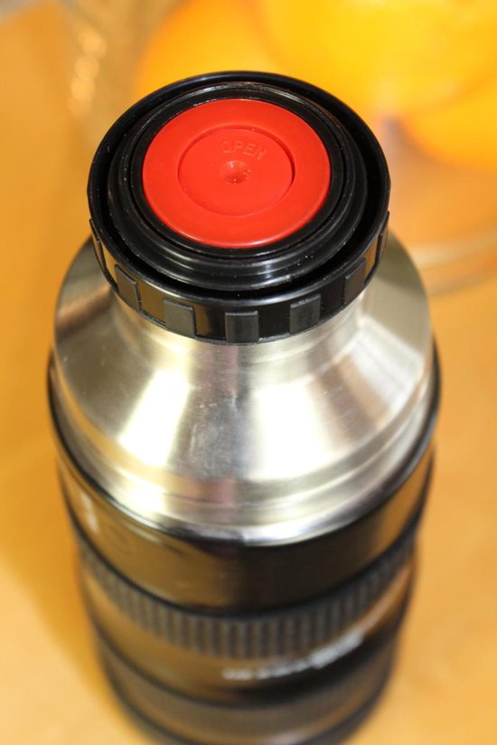 Close-up van de rood met zwarte dop van een thermosfles in de vorm van een cameralens.
