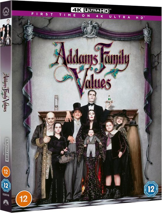De Addams Family, gekleed in hun kenmerkende zwarte kleding, poseren voor een open haard. Familievaders Gomez en Fester in de achterhoede.