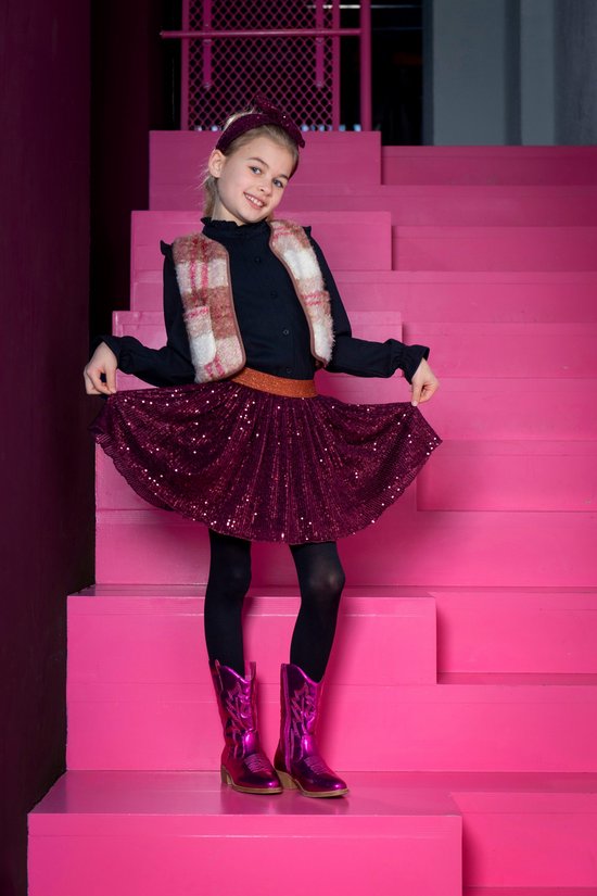 Meisje in zwart hemd, vest met ruitpatroon, bordeauxrode pailletten rok, legging en roze laarzen.