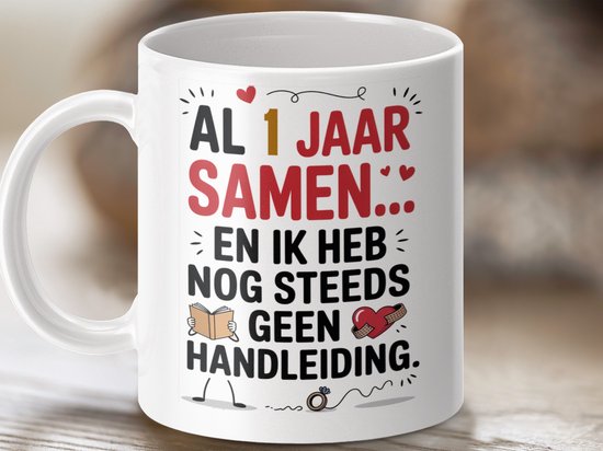 Witte mok met tekst 'AL 1 JAAR SAMEN... EN IK HEB NOG STEEDS GEEN HANDLEIDING.' op een houten achtergrond.