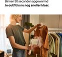 Vrouw in groene T-shirt gebruikt een beige Braun QuickStyle 3 kledingstomer op een bruine jas.