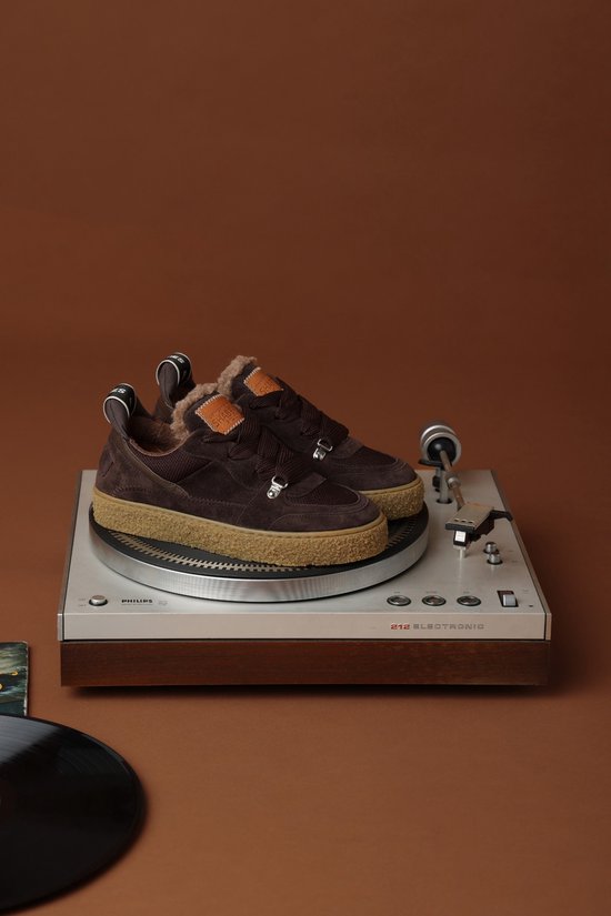 Donkerbruine suède sneakers met bontvoering, gepresenteerd op een platenspeler.