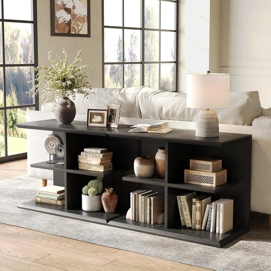 Zwarte consoletafel met open vakken, gevuld met boeken, vazen en decoratieve objecten, in een woonkamer met grote ramen.