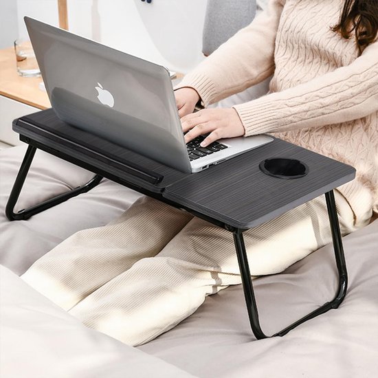 Vrouw op bed met een donkergrijs houten laptoptafel op schoot. Tafel met bekerhouder en laptop.