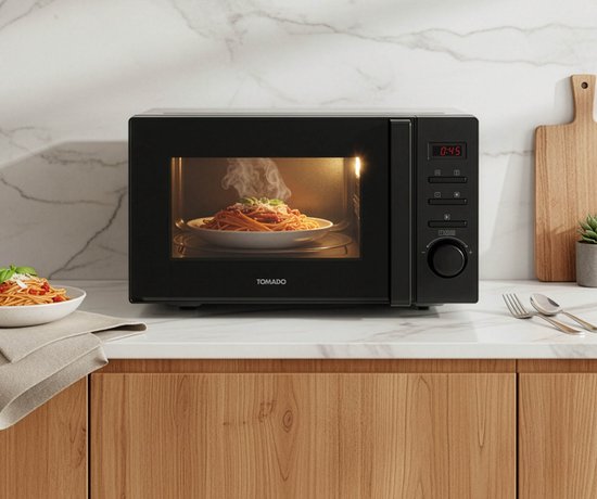 Micro-ondes noir Tomado avec une assiette de spaghettis fumants à l'intérieur, posé sur un comptoir.