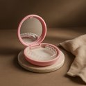 Roze beugendoosje met spiegel, liggend op een marmeren schijf met een beige doek ernaast.