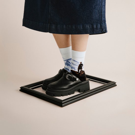 Model draagt een spijkerrok en zwarte klomp-sneakers met witte sokken met berglandschap.