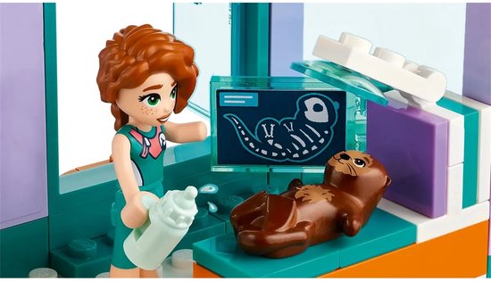 Autumn met een flesje bij een zeeotter in het LEGO Friends Reddingscentrum. De otter ligt op een onderzoekstafel.