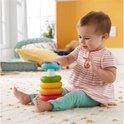 Baby zit op de grond en speelt met een Fisher-Price stapelpiramide met vijf gekleurde ringen. Ze probeert een ring op te zetten.