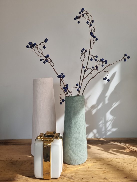 Lichtroze vaas met steenachtig oppervlak naast een groene vaas met takken met blauwe bessen en een wit cadeau met gouden strik.